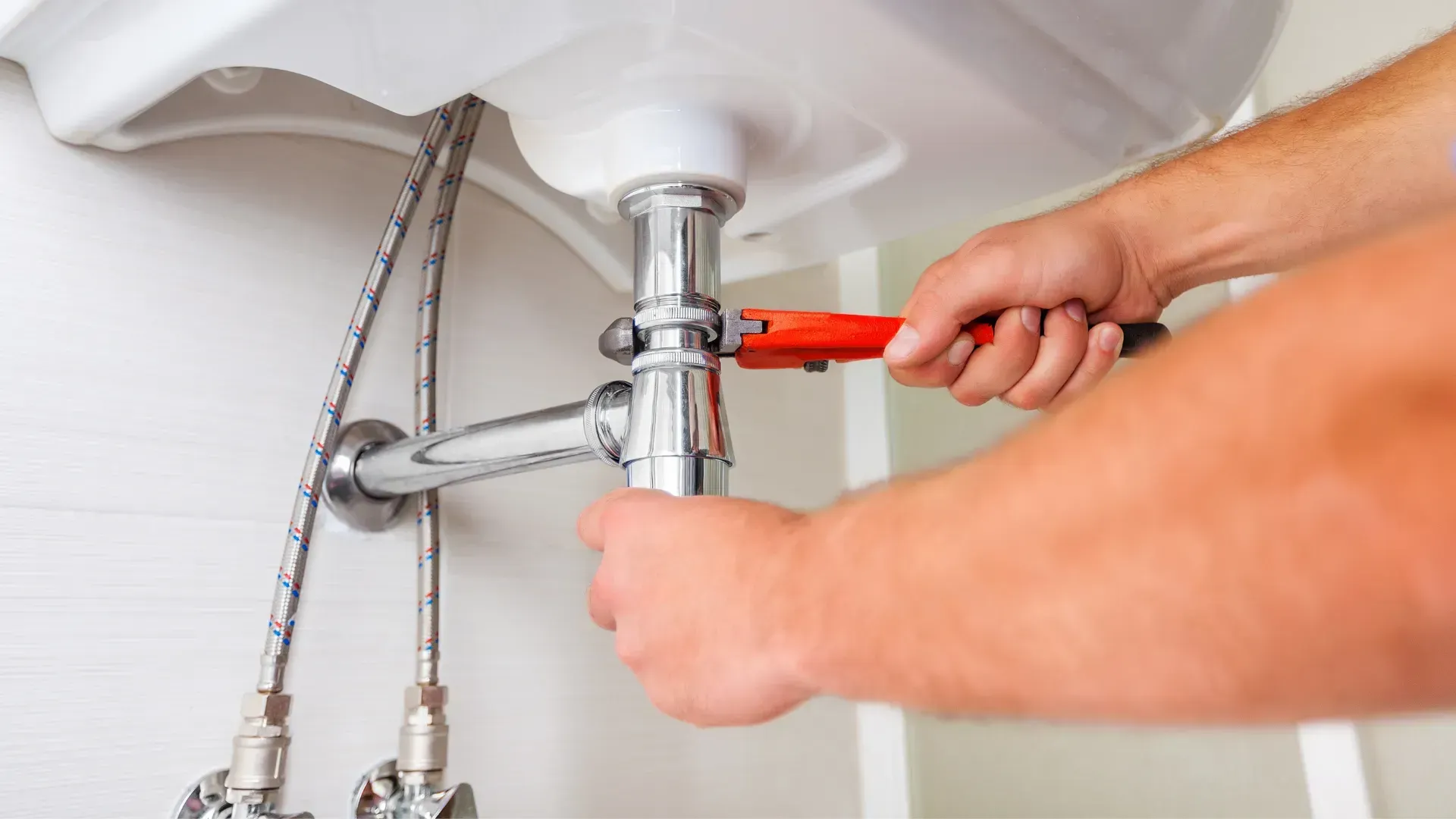 A plumber is fixing a sink pipe with a wrench.