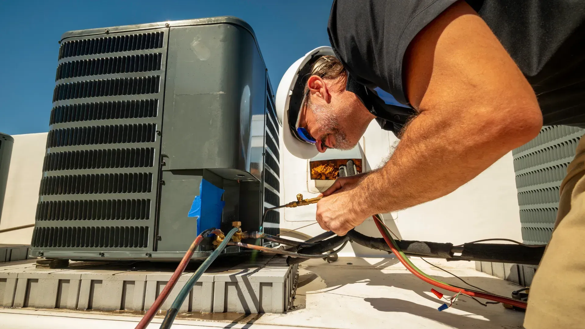 A man is working on an air conditioner on top of a building.