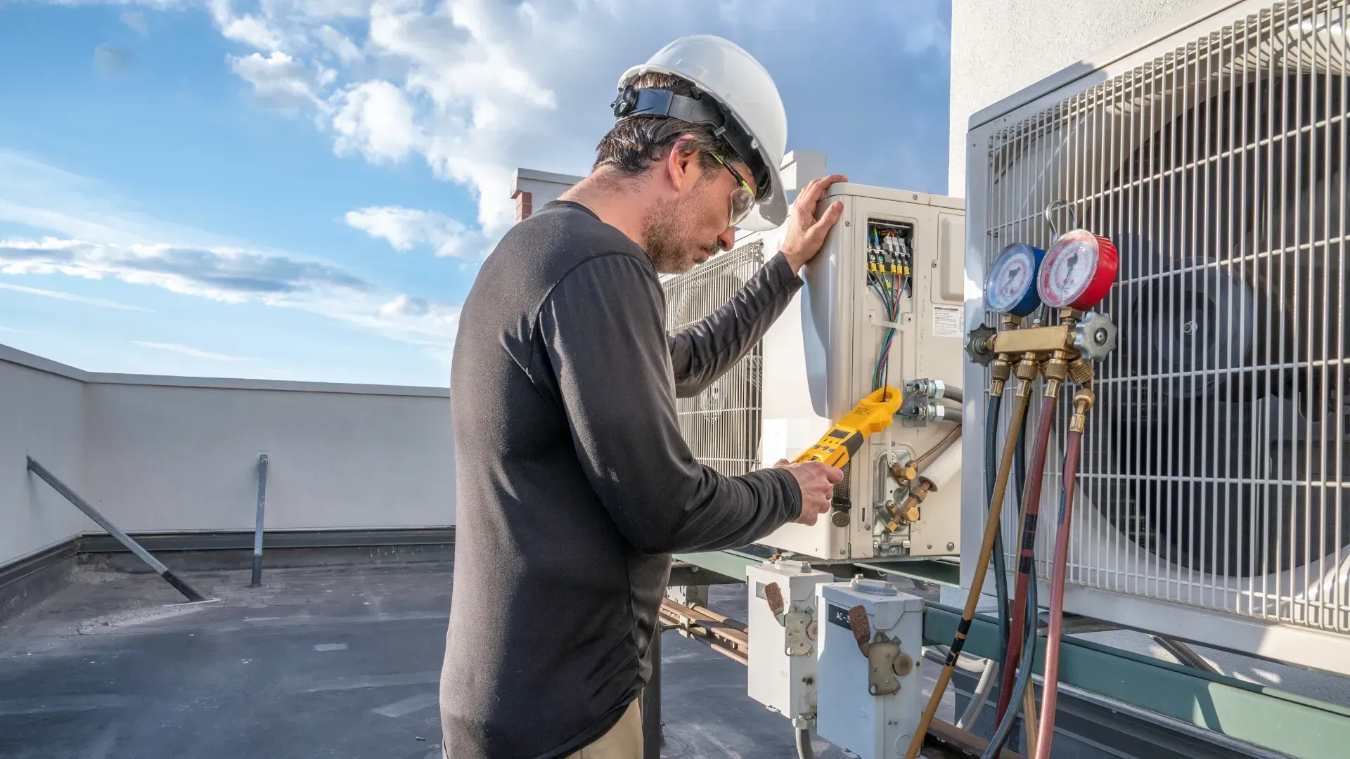 A man is working on an air conditioner on the roof of a building.