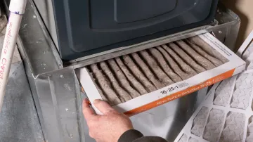 A person is cleaning a dirty air filter on a furnace.