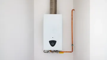 A white water heater is hanging on a white wall next to a copper pipe.