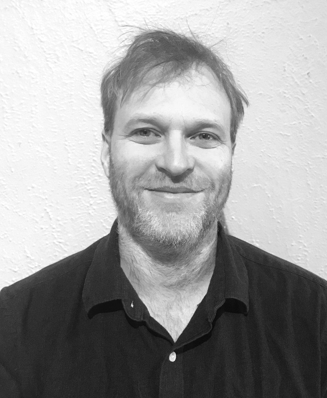 Un homme barbu sourit sur une photo en noir et blanc.