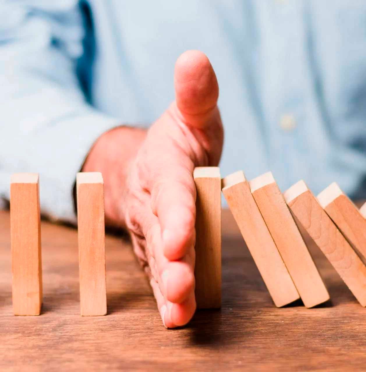 Main empêchant des dominos en bois de tomber sur une table en bois.