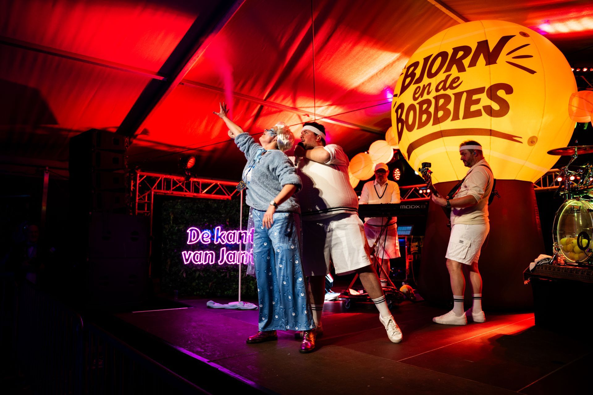 Band op het podium onder rode lichten; groot opblaasbaar logo 