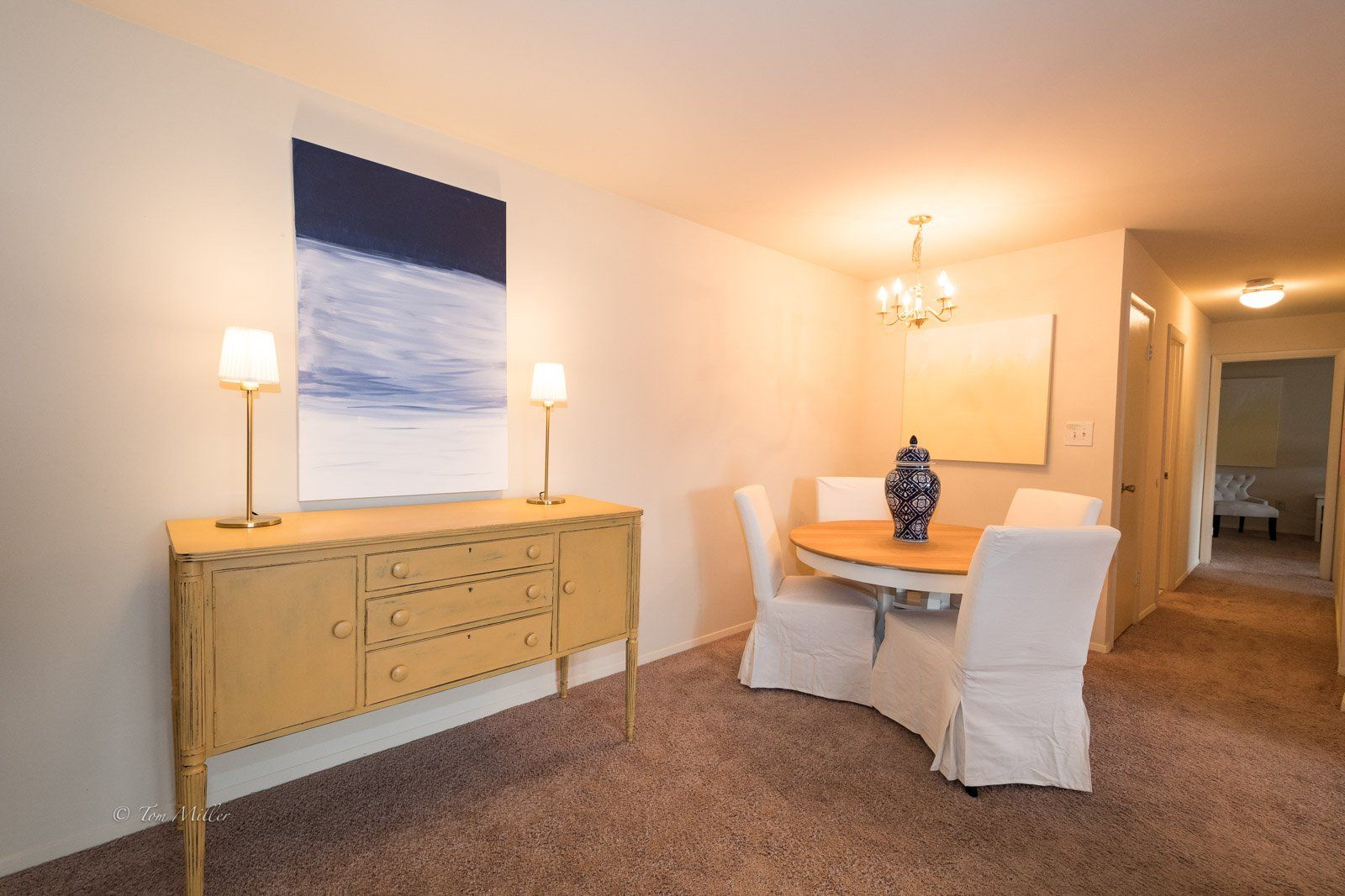 The dining area with white chairs, a chandelier, and dresser
