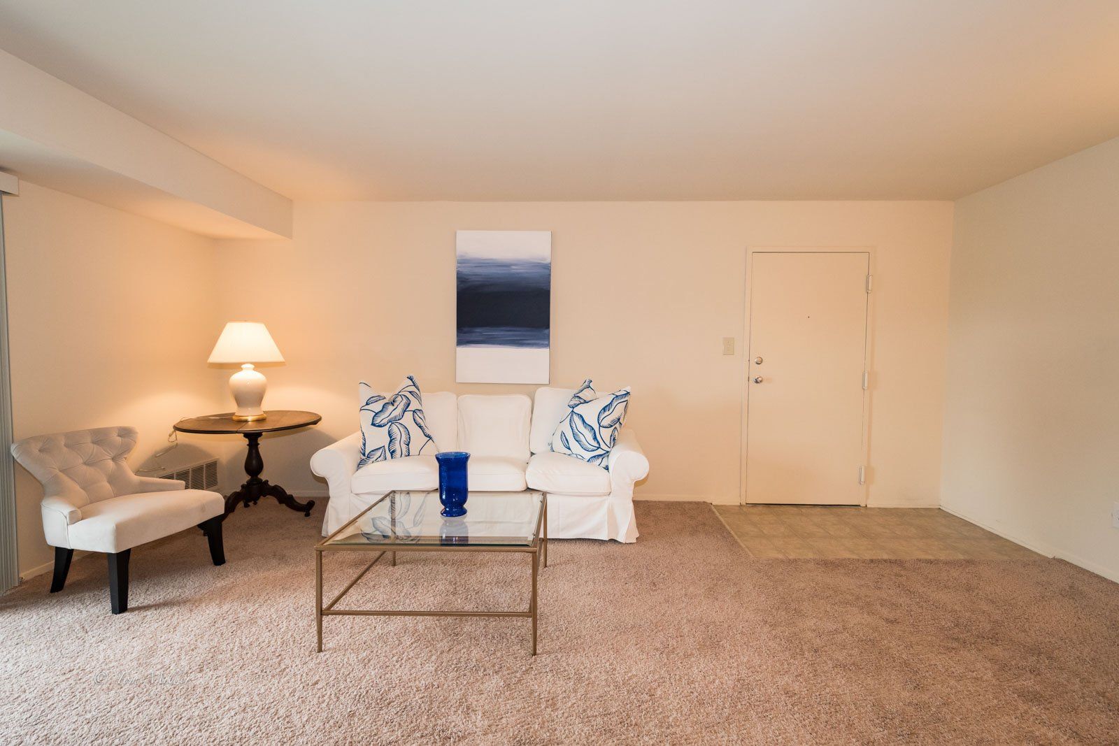 A white couch with glass coffee table and blue vase