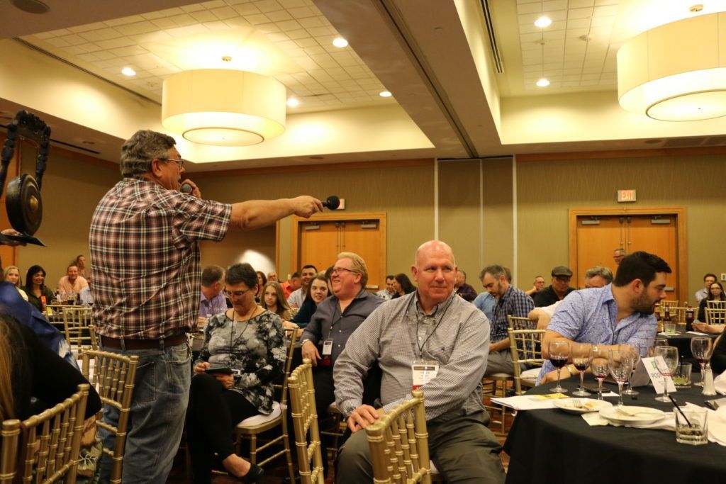 A man is pointing at a group of people sitting at tables in a conference room.