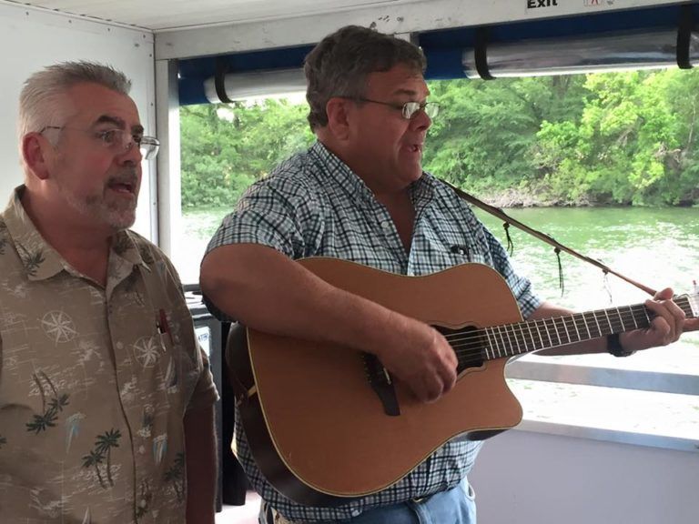 Two men singing and playing guitars on a boat