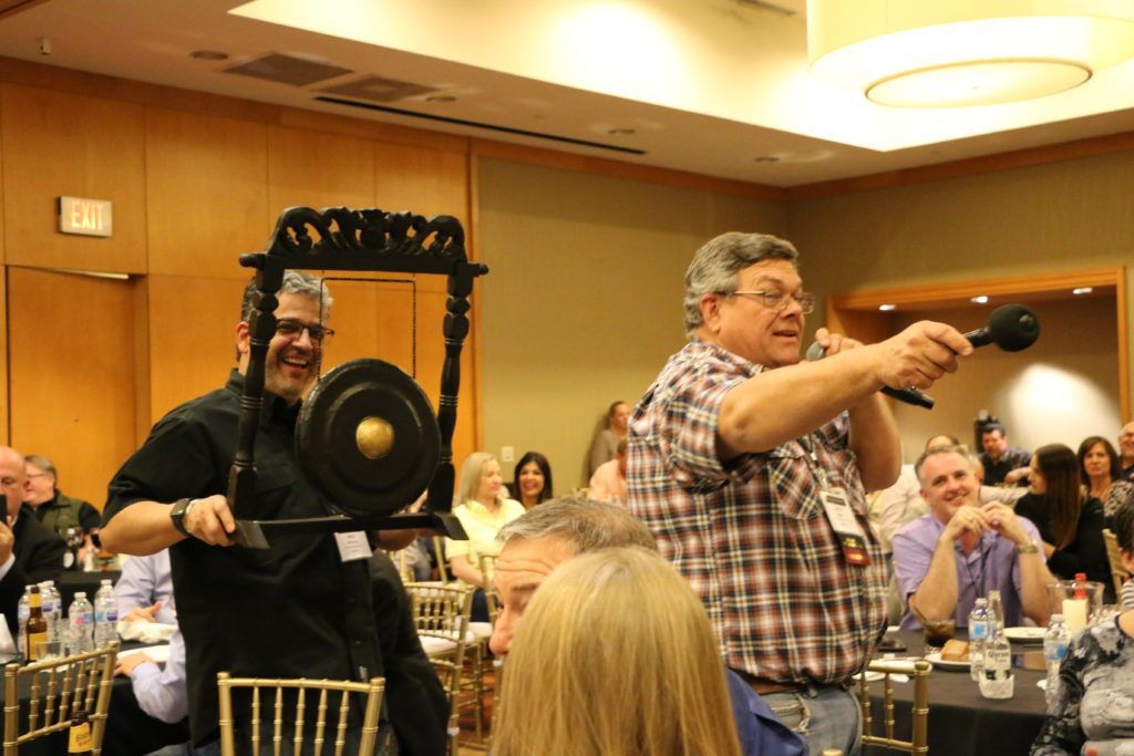 A man is holding a gong and a microphone in front of a group of people.