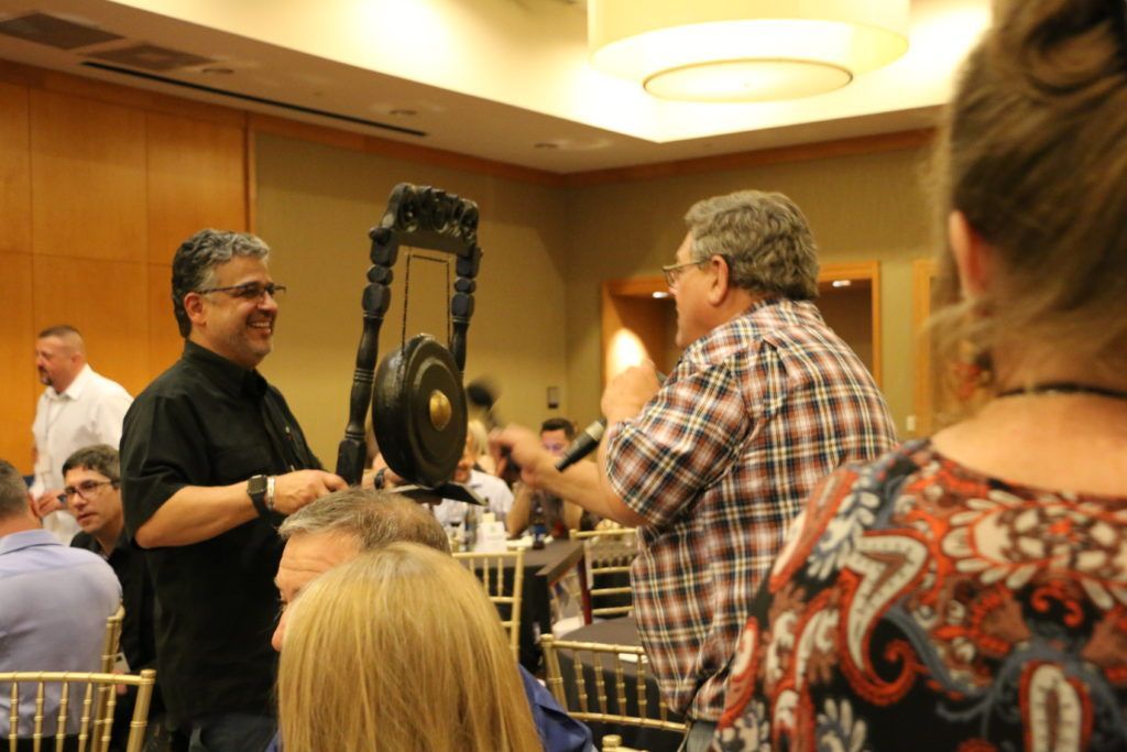 A man is playing a gong in front of a group of people.