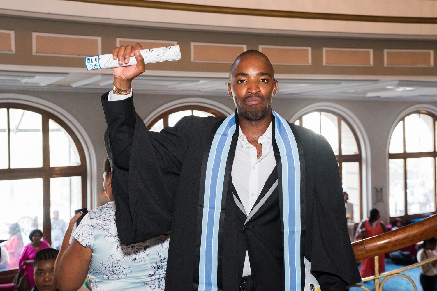 A man in a graduation cap and gown is holding a diploma in his hand.