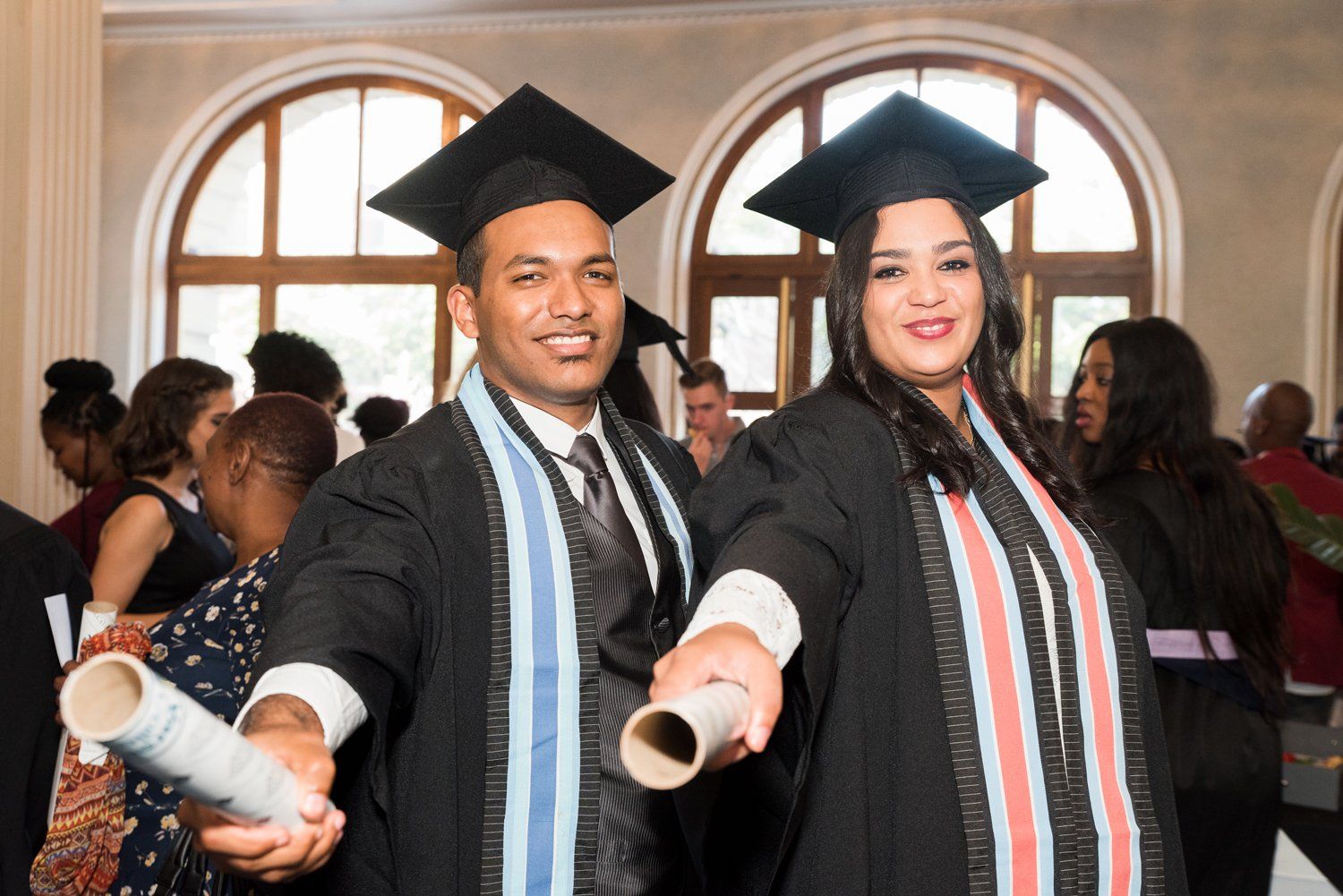 A man and a woman in graduation caps and gowns are holding a diploma.