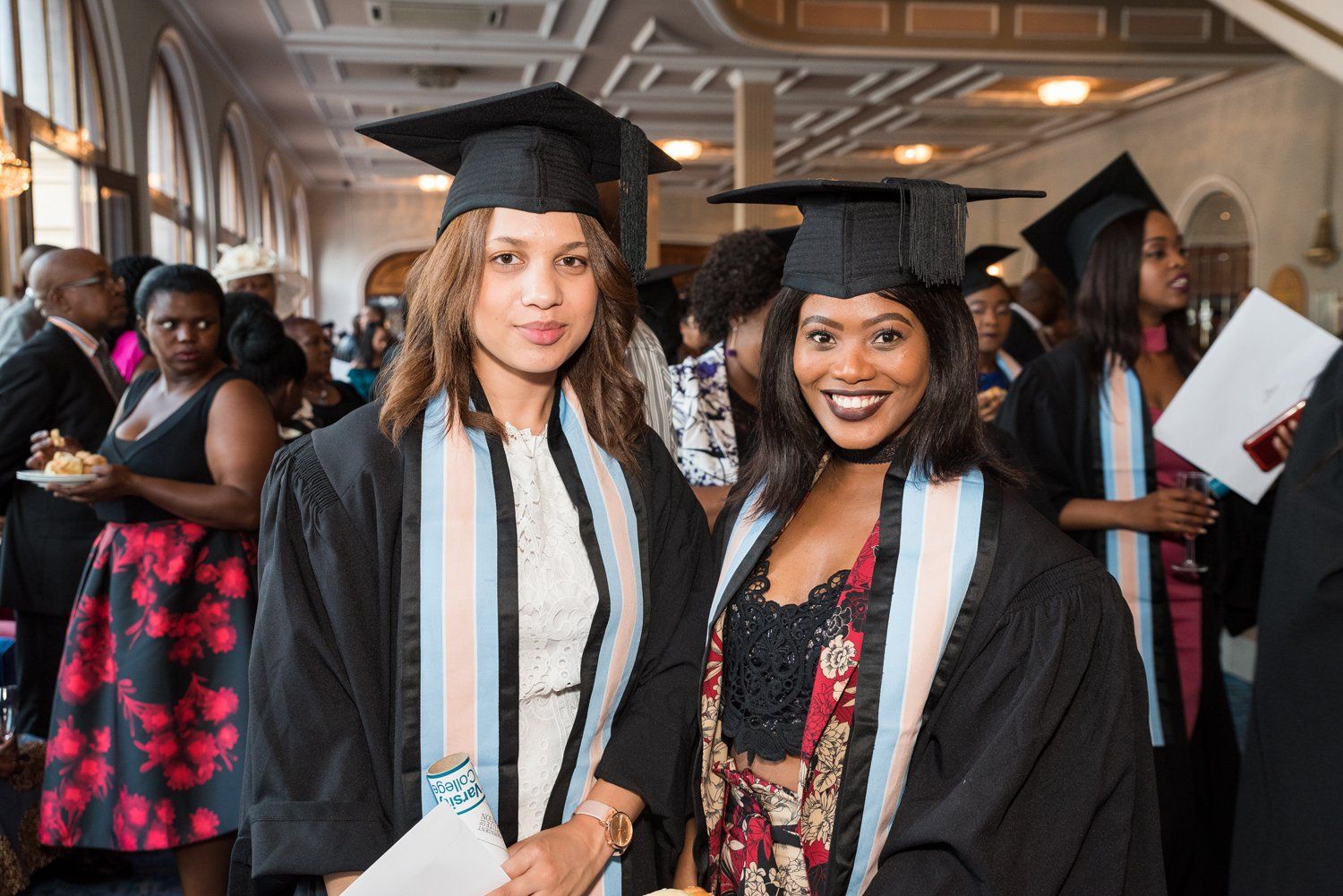 Two female graduates are standing next to each other at a graduation ceremony.