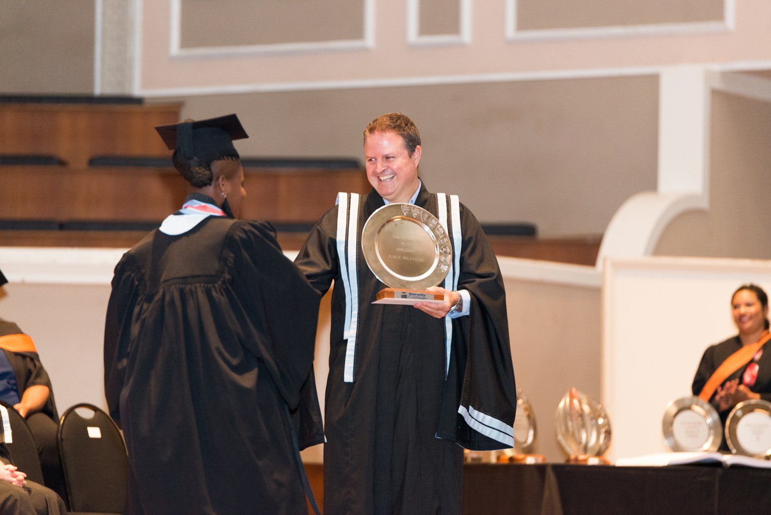 A man in a graduation cap and gown is shaking hands with another man