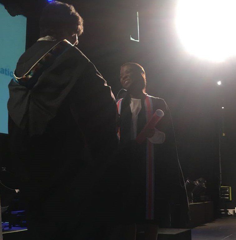 A man in a graduation cap and gown speaks into a microphone