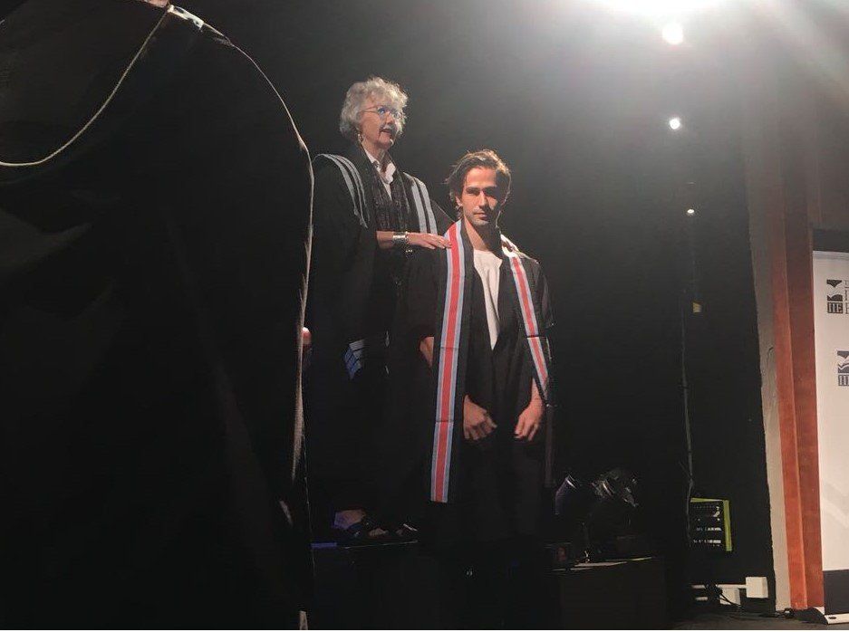 A man in a cape stands next to another man on a stage