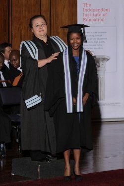 A woman in a graduation cap and gown stands next to another woman