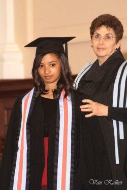 A woman in a graduation cap and gown stands next to another woman