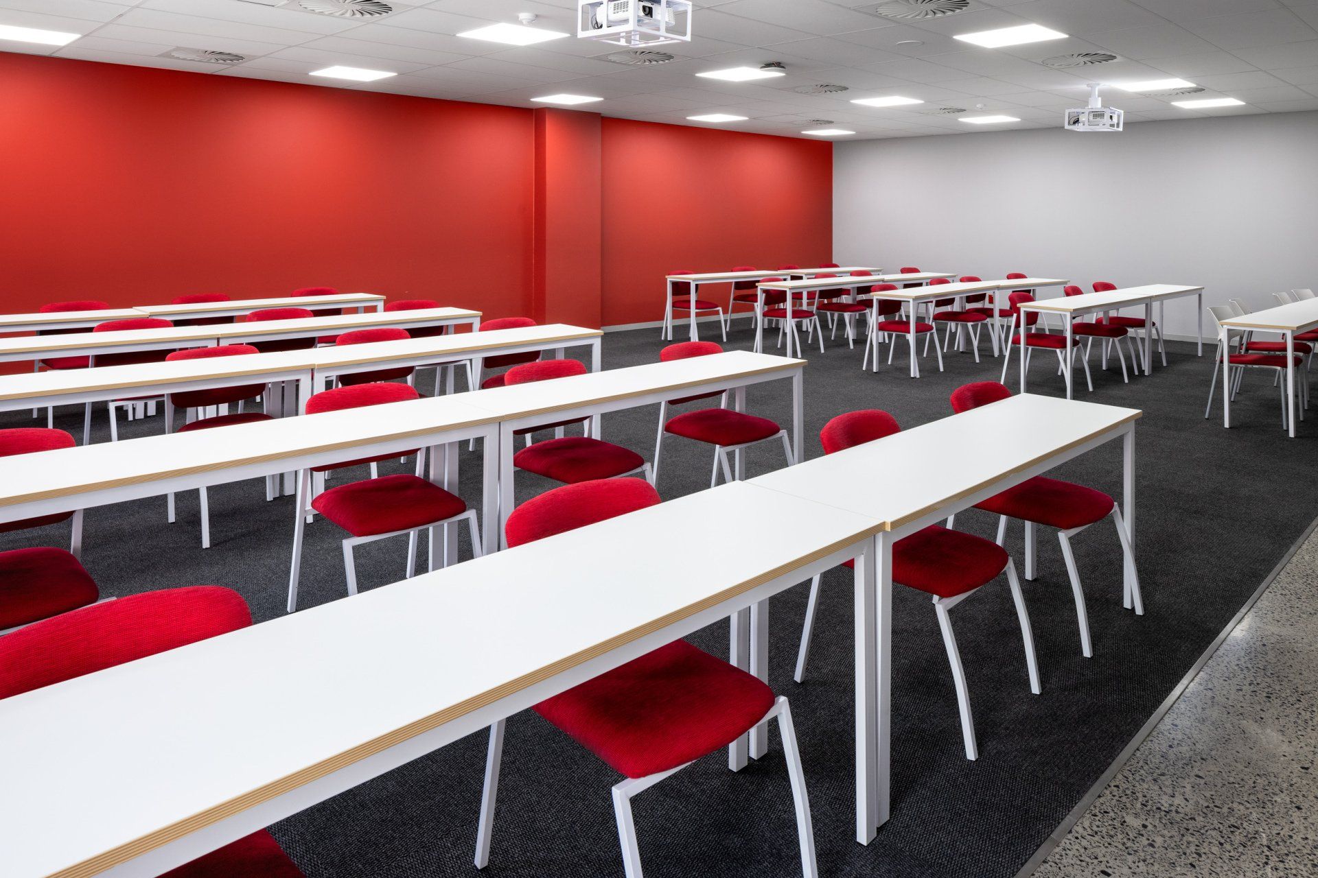 A classroom with long white tables and red chairs