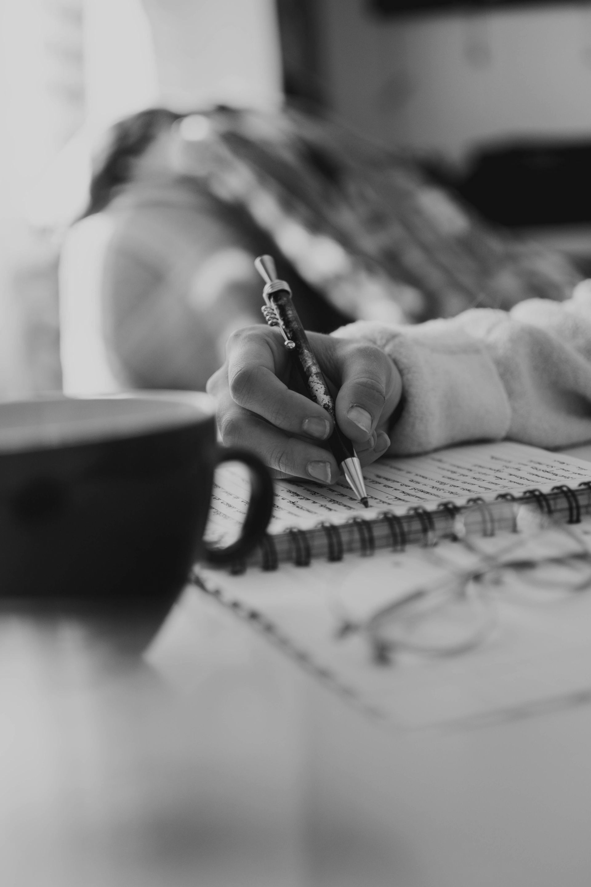 A person is writing in a notebook next to a cup of coffee.
