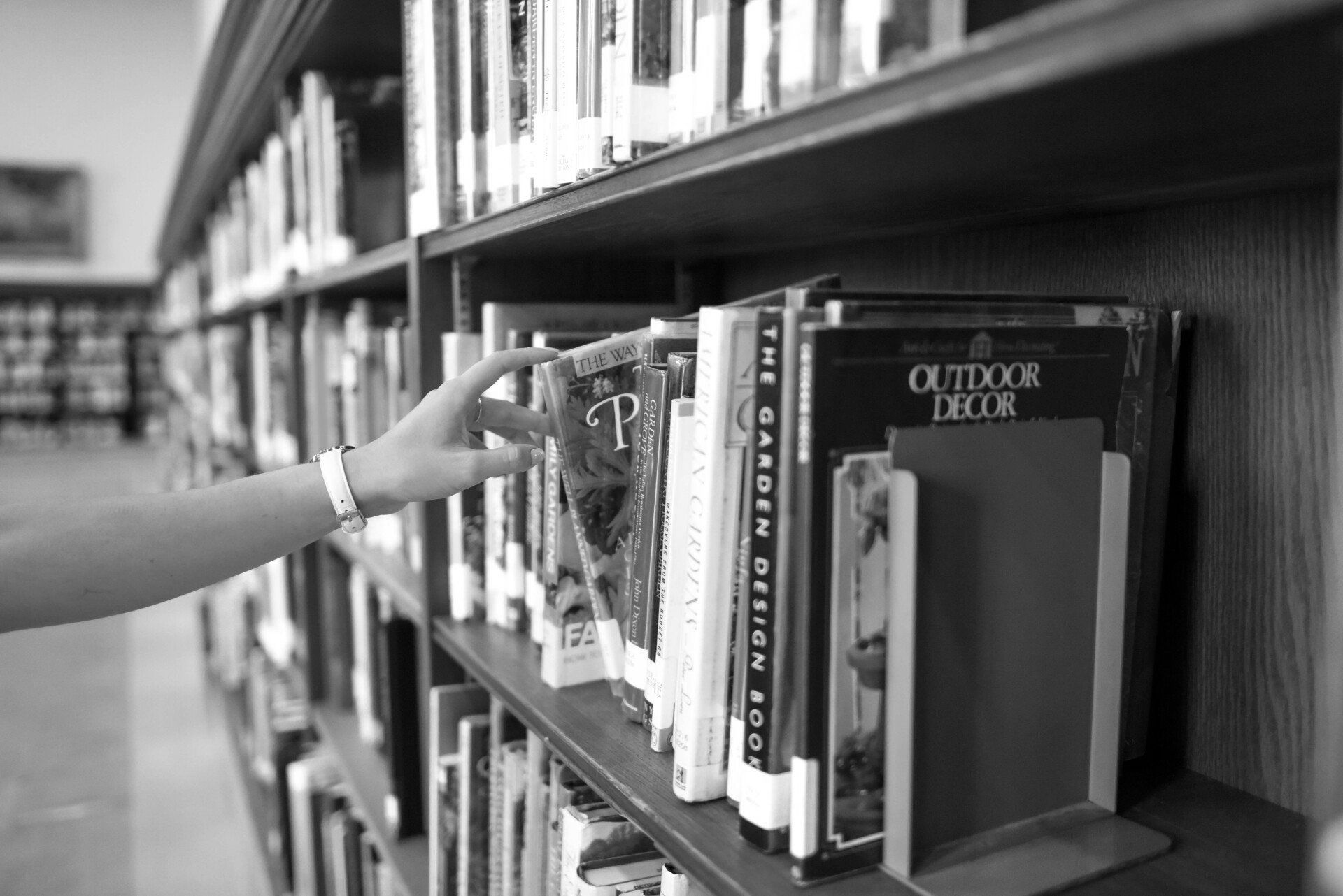 A person is reaching for a book on a library shelf.