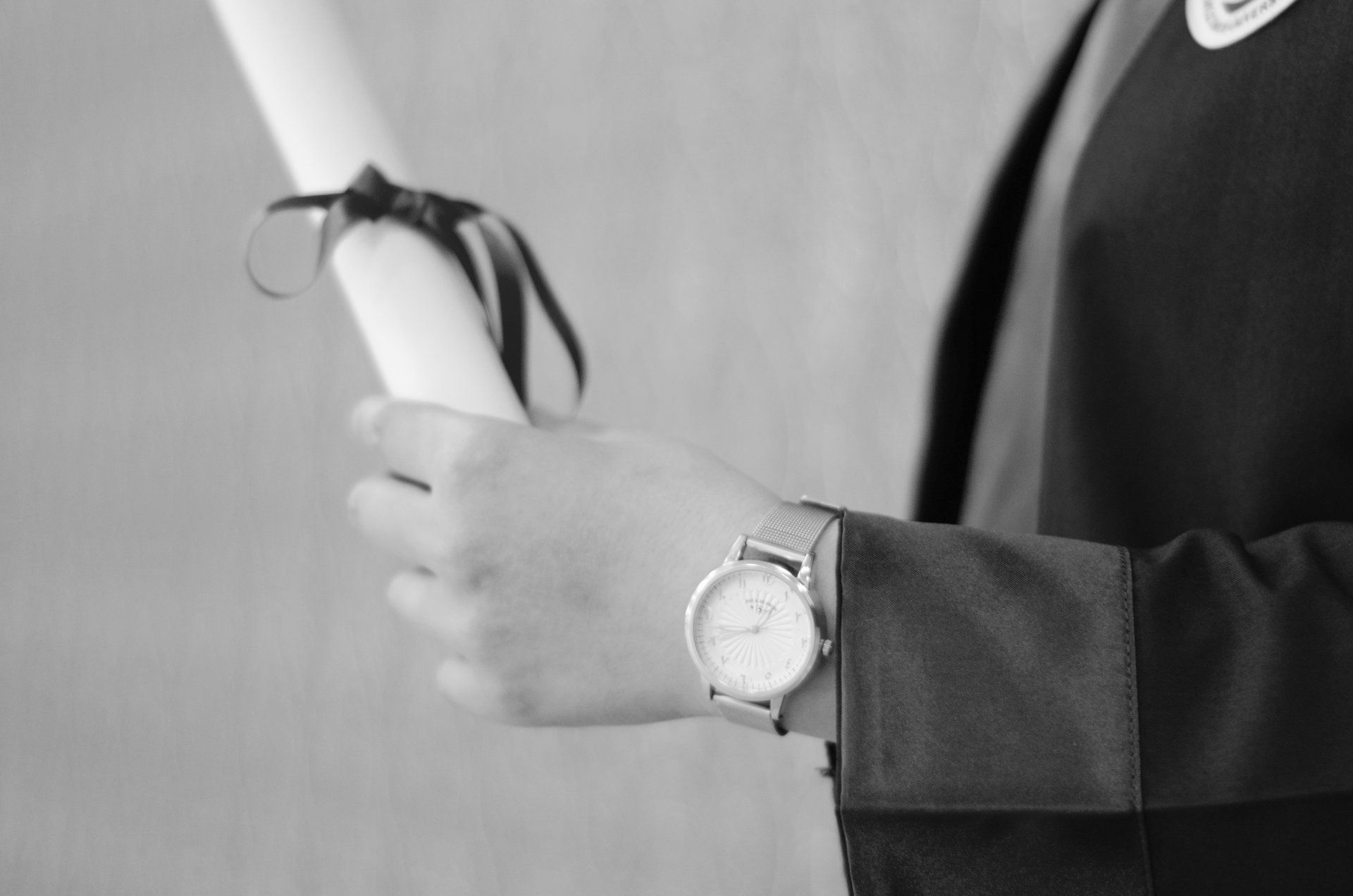 A person wearing a watch is holding a diploma in their hand.