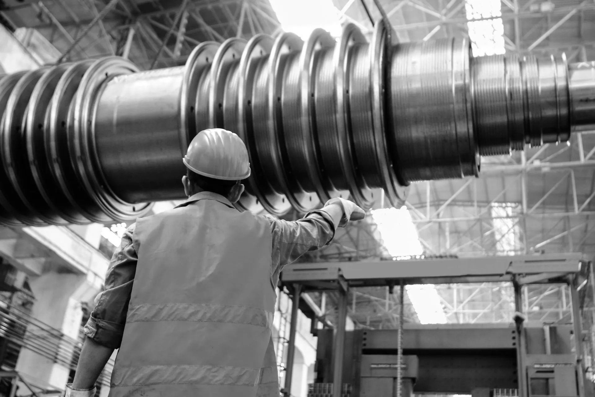 A man wearing a hard hat is working on a large metal object in a factory.