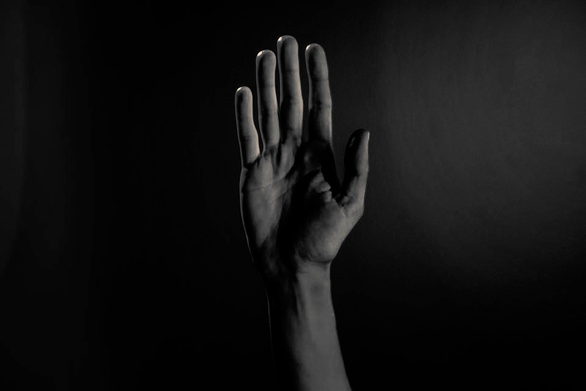 A black and white photo of a hand reaching up in the dark.