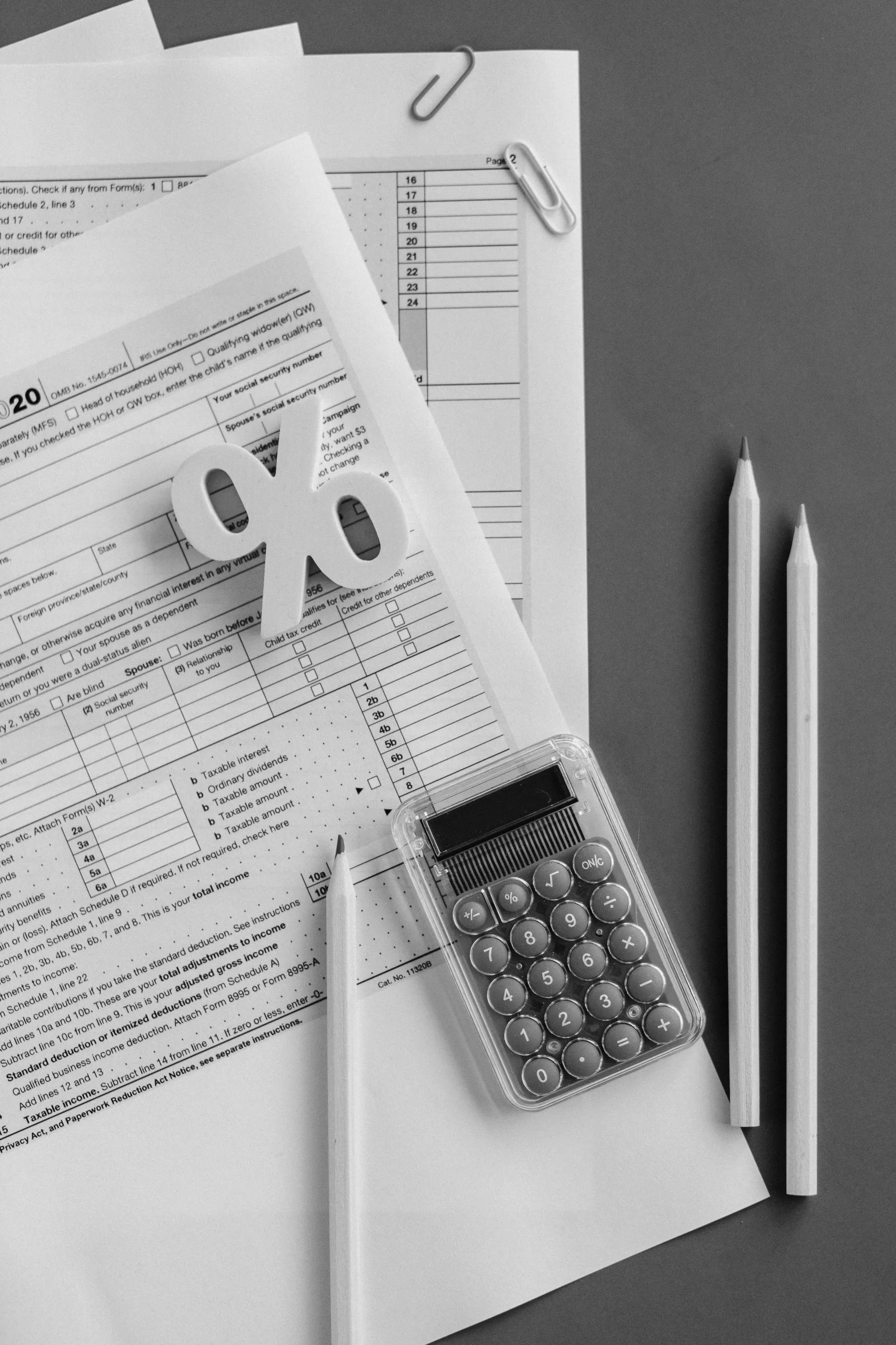 A black and white photo of a calculator , pencils , and papers.