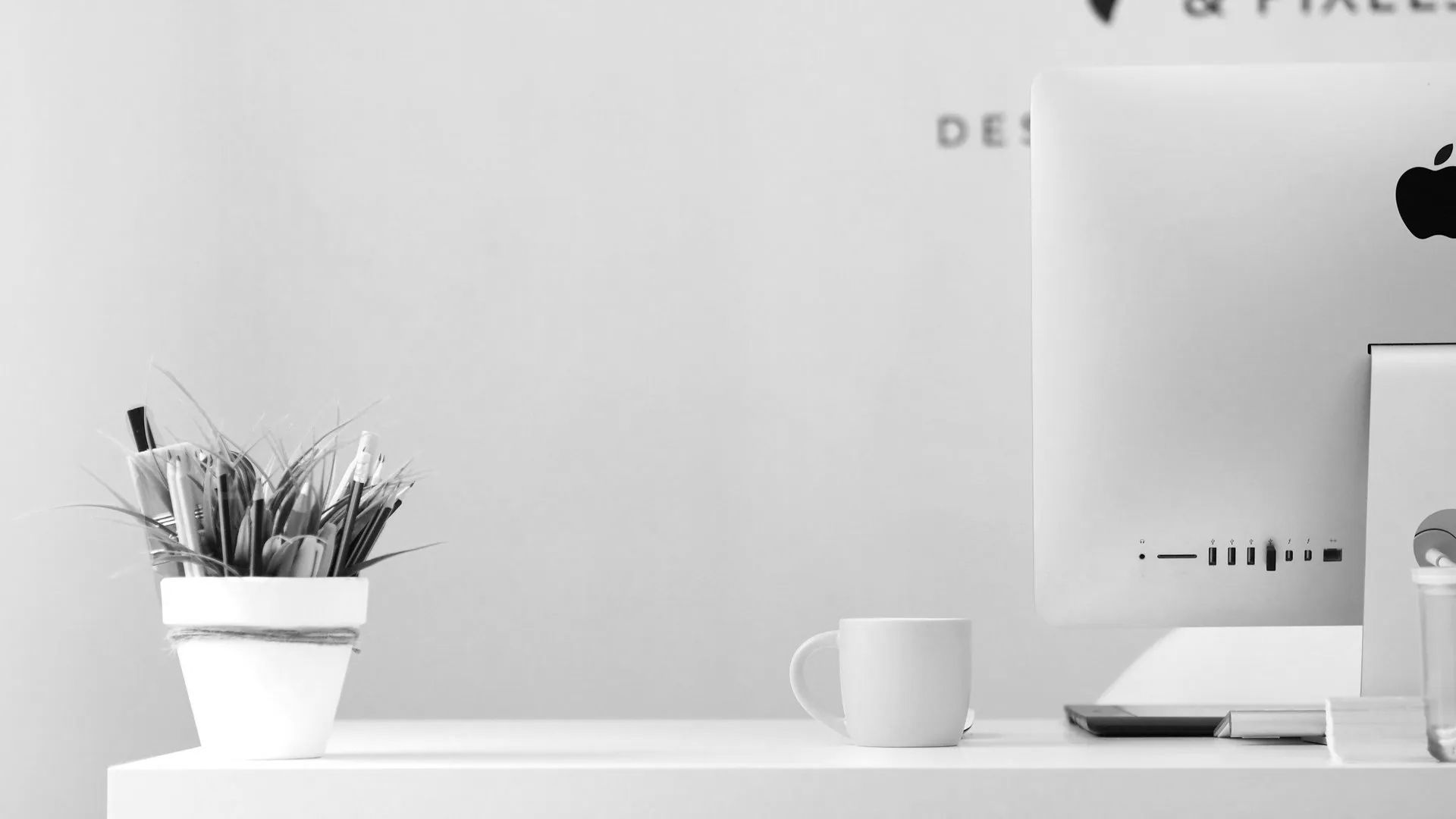 A black and white photo of a desk with a computer and a potted plant.