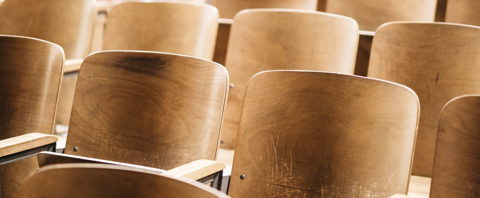 A row of empty wooden chairs in an auditorium.