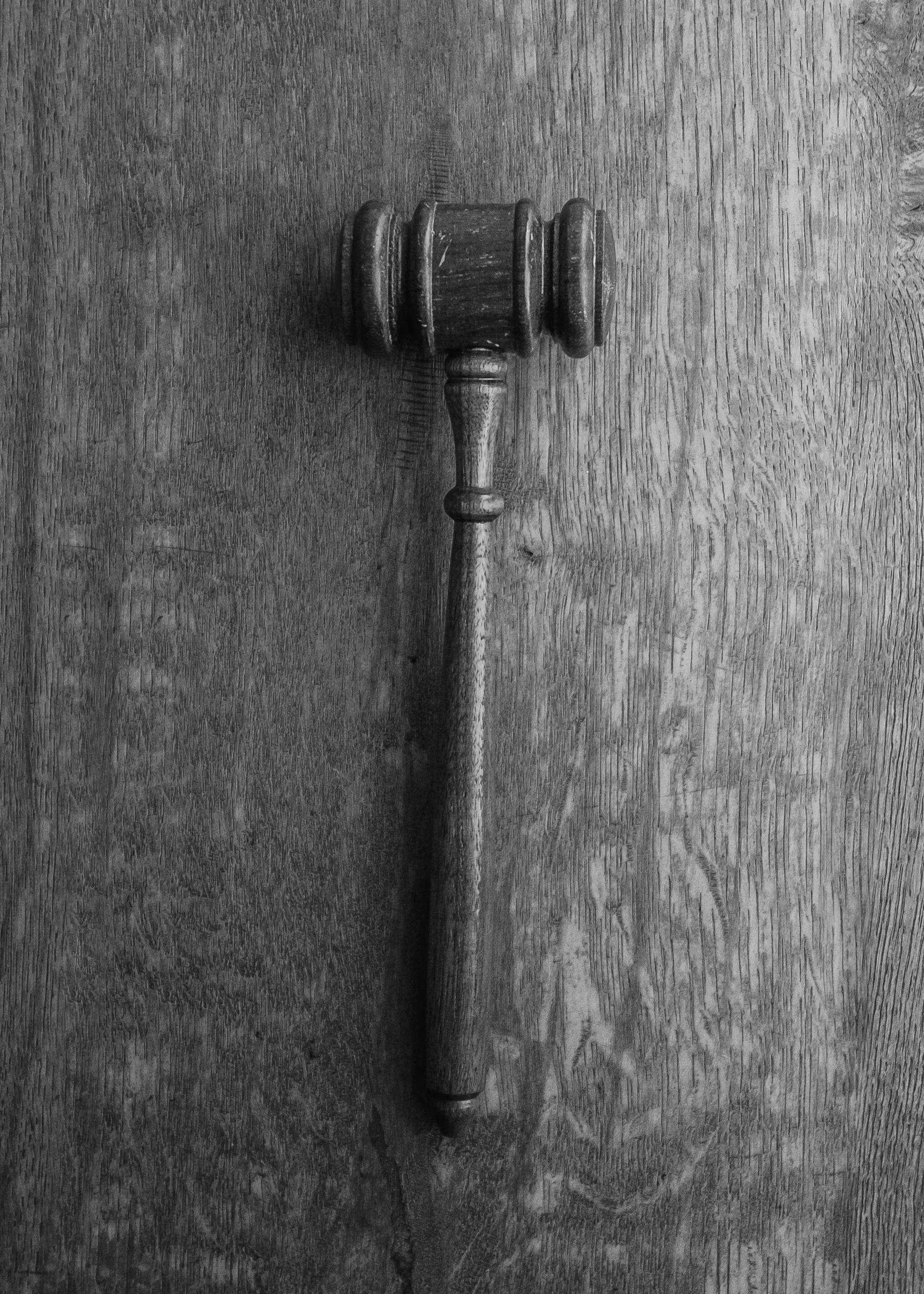 A black and white photo of a wooden judge 's gavel on a wooden table.