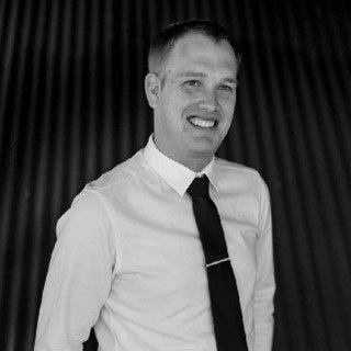 A man in a white shirt and black tie is smiling in a black and white photo.