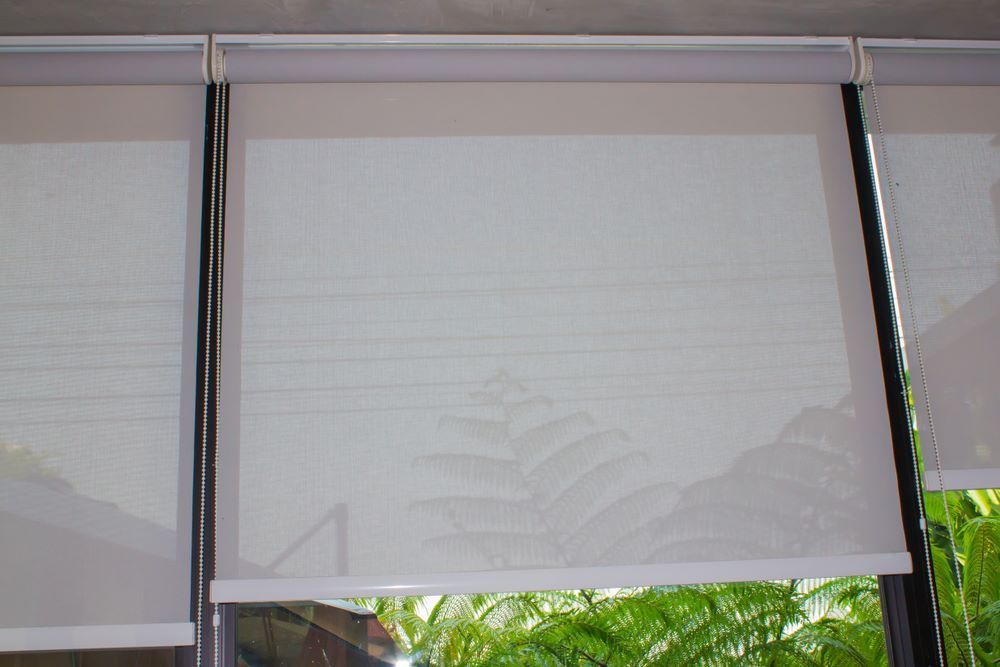 A Close Up of a Window With White Roller Blinds on It — Aussie Carpets & Vinyl In Buderim, QLD