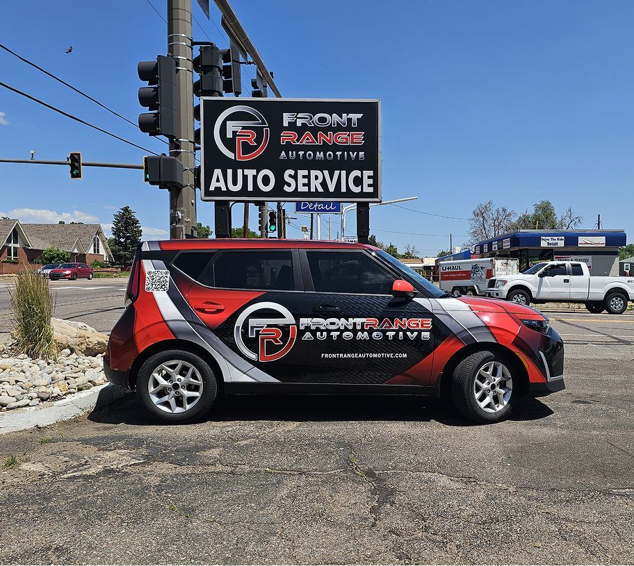 A red Kia Soul with Front Range Automotive logo parked in front of their sign. | Front Range Auto
