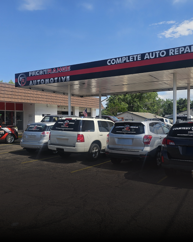 A row of cars parked in front of an automotive repair shop with a black, red, and white awning under a blue sky. | Front Range Auto