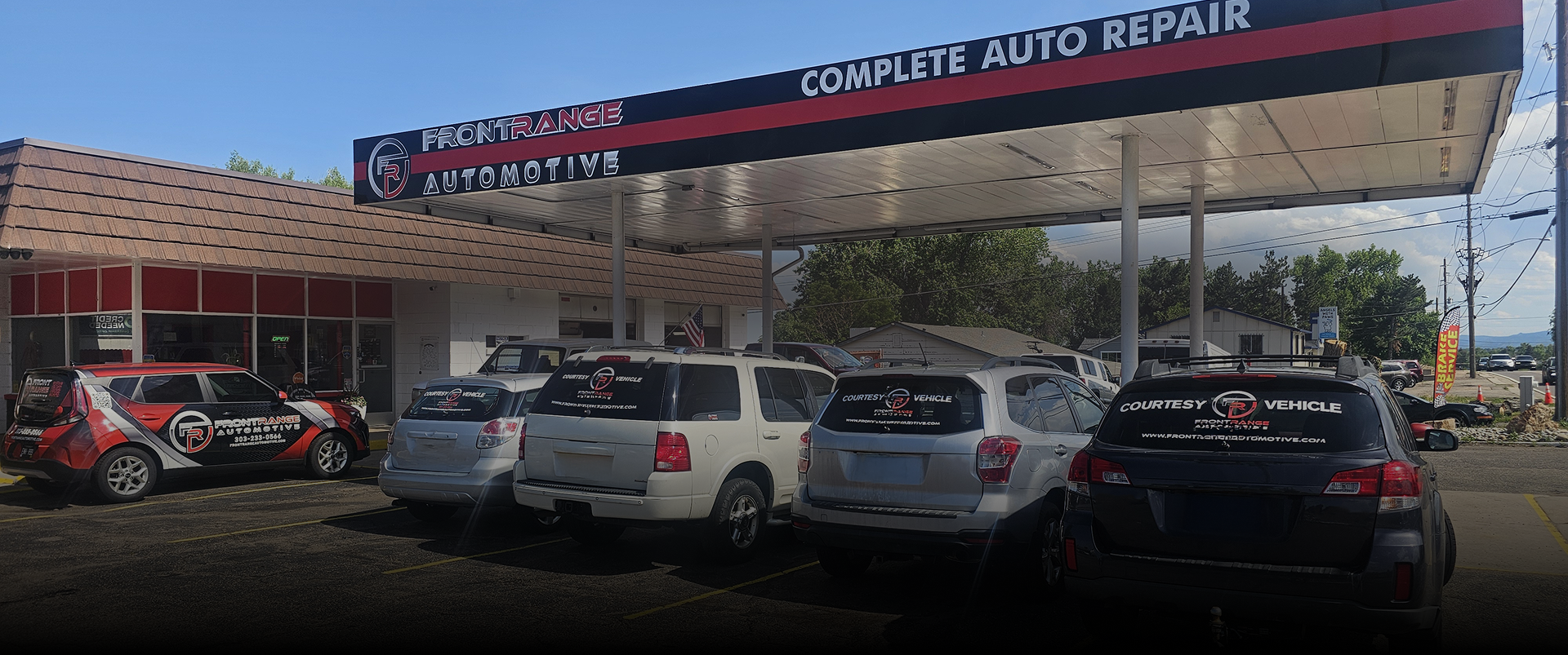 Auto repair shop with parked cars under a canopy and in front. Sign reads 
