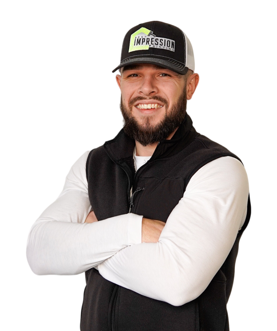 A man with a beard wearing a hat and vest is standing with his arms crossed.