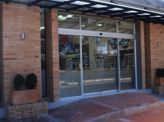 Puertas automáticas correderas de cristal con fachada de ladrillo y toldo.