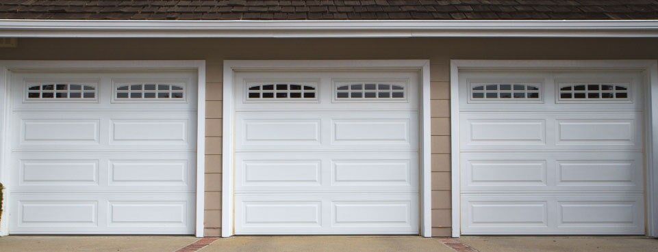 Tres puertas de garaje blancas con paneles de vidrio en una casa de color beige claro.
