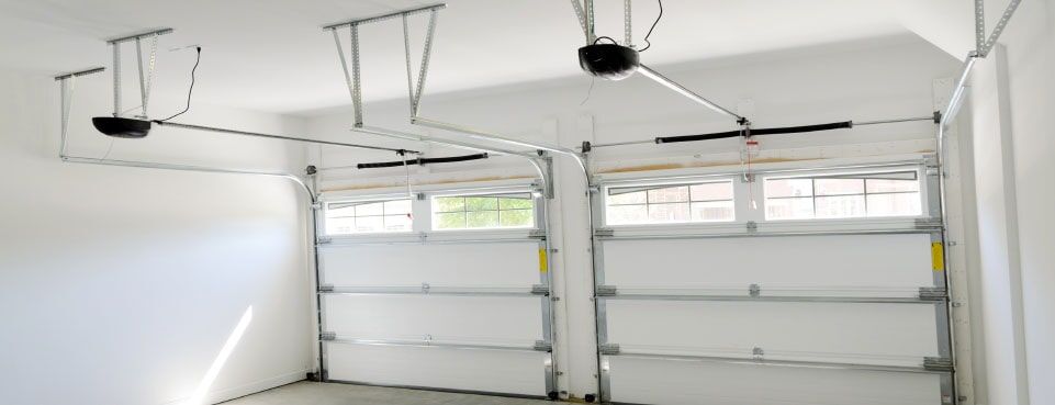 Vista interior de un garaje con dos puertas de garaje blancas abiertas y mecanismos de apertura superiores.