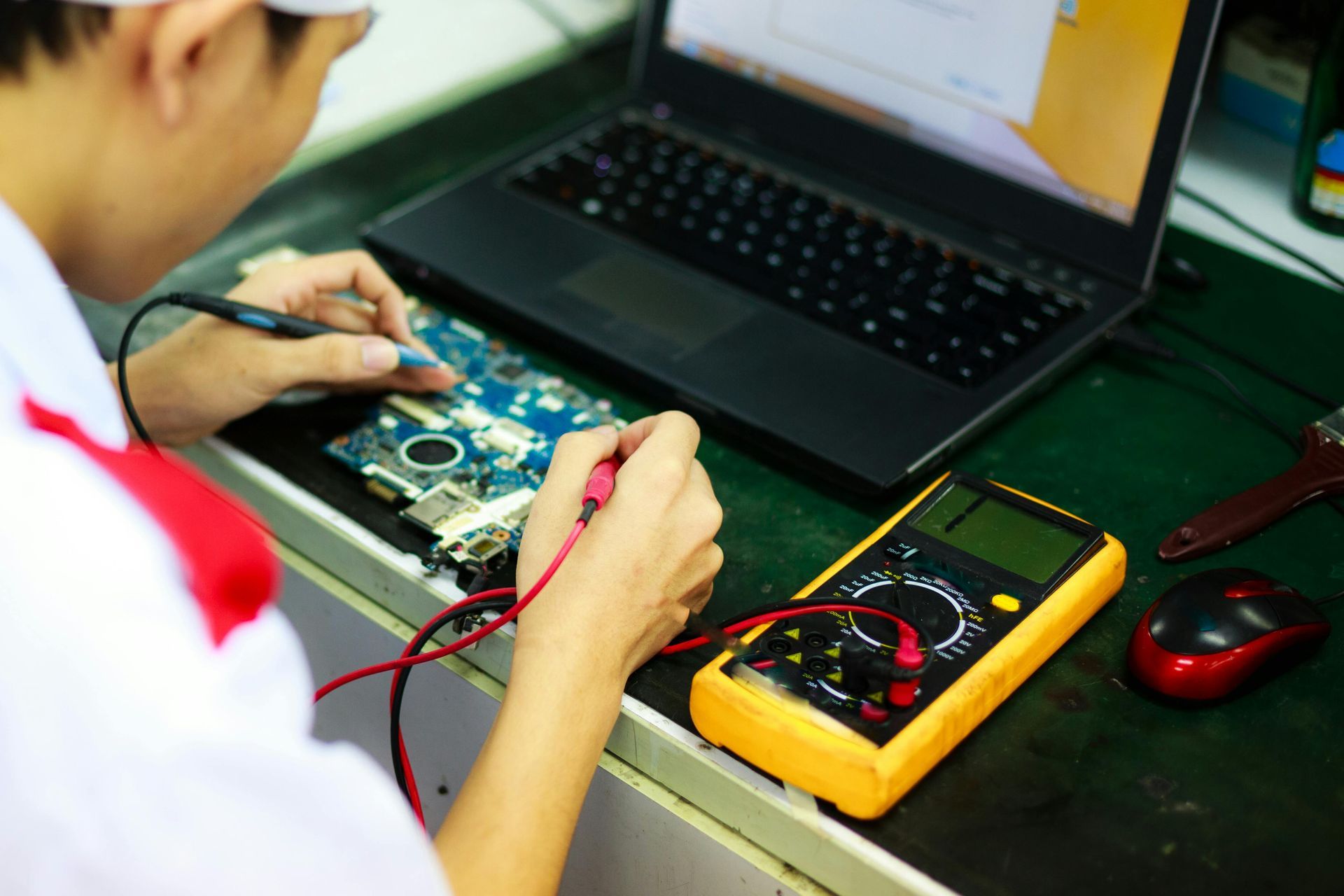 A man is working on a laptop with a multimeter