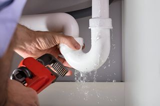 A plumber is fixing a leaking sink pipe with a wrench.