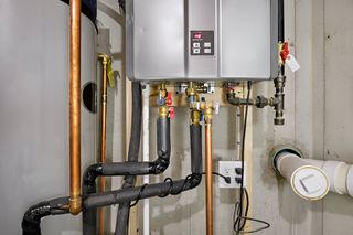 A water heater is sitting on a wall next to a bunch of pipes.