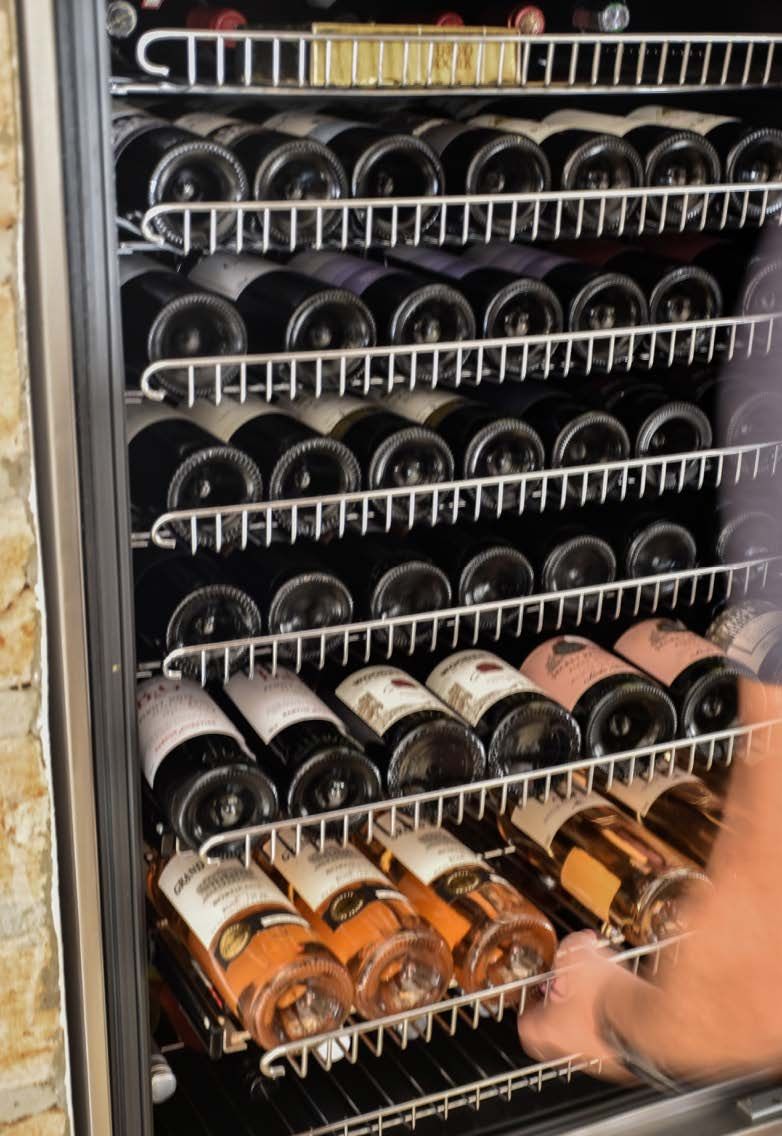 Uma pessoa está segurando uma garrafa de vinho em um refrigerador de vinho.