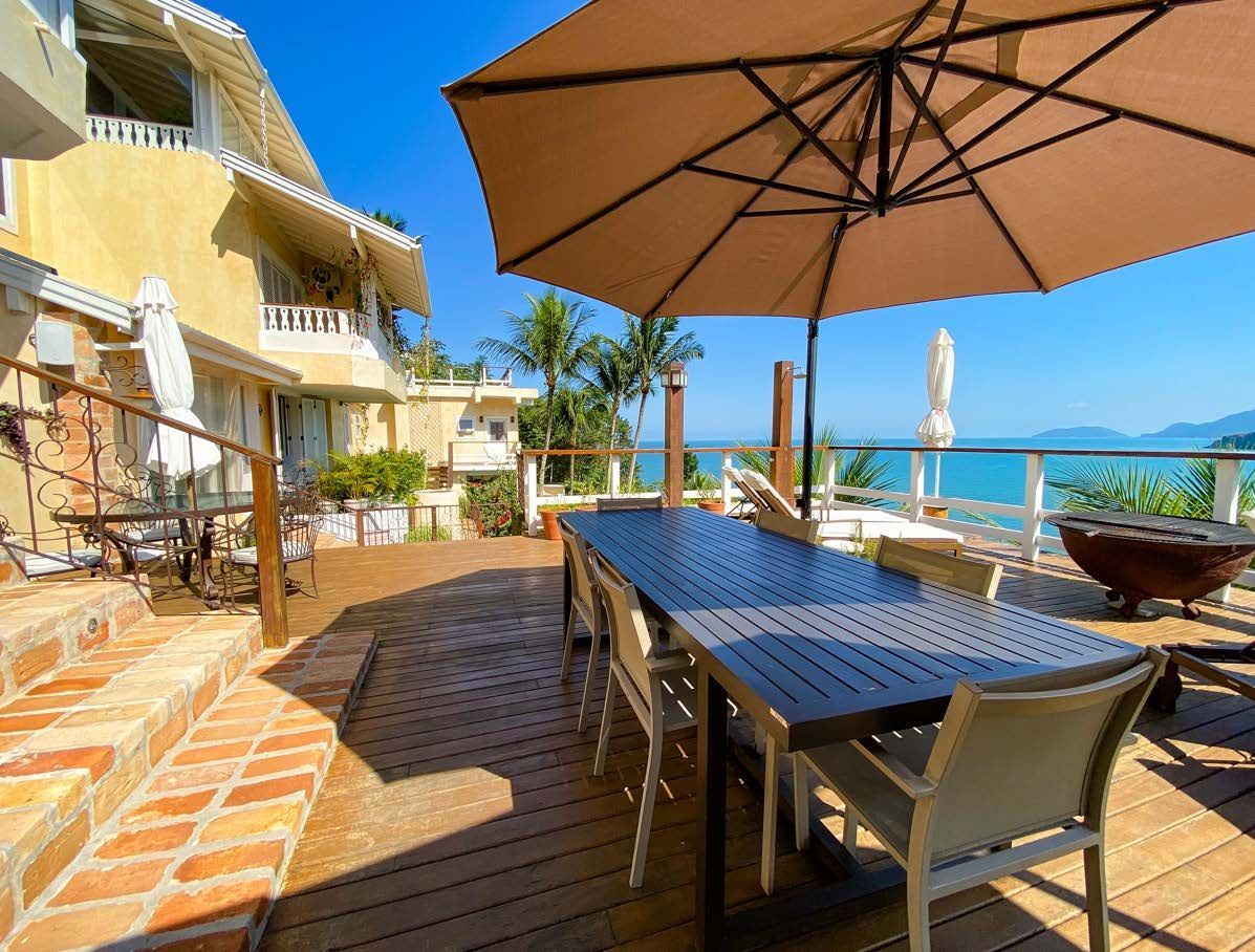 Uma grande mesa com cadeiras e guarda-sóis em um deck com vista para o oceano.