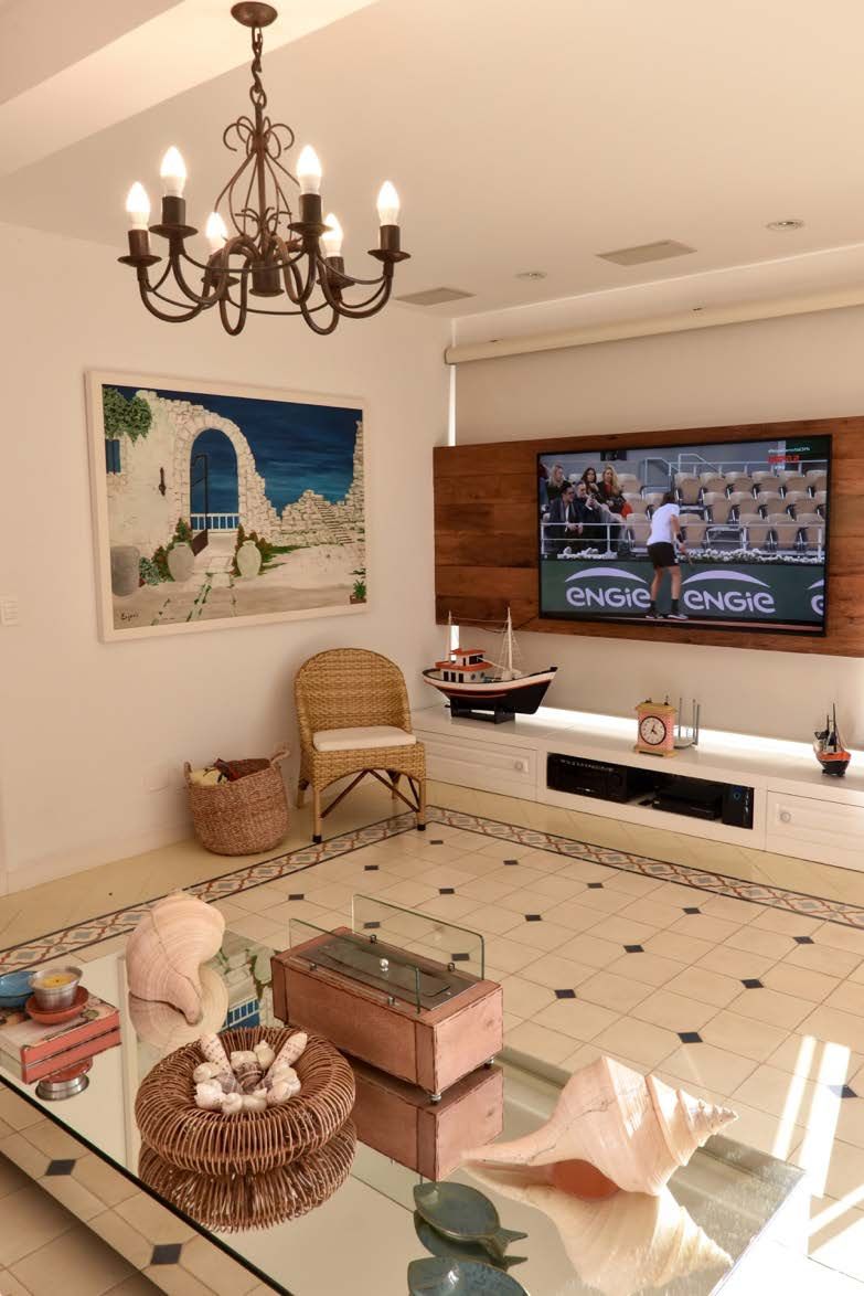 Uma sala de estar com uma mesa, cadeiras, uma televisão e um lustre.