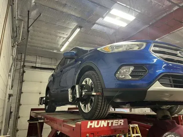Blue SUV on a red lift in a garage, undergoing a wheel alignment with Hunter equipment.