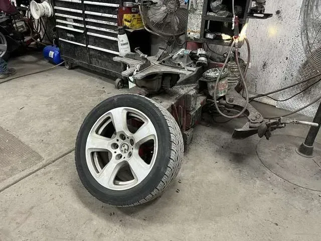 Wheel and tire in a mechanic's shop, near tools and equipment; a white wheel with a tire lies on the floor.