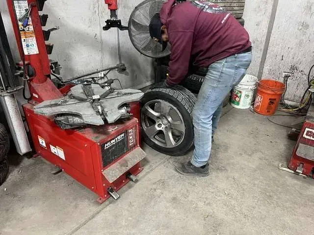 A person changing a tire in a garage. They are using a tire machine, with the tire and wheel on the ground.